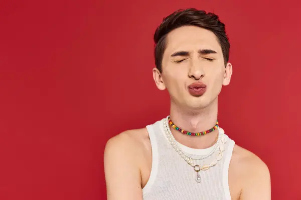 Attrayant jeune homme gay en tenue blanche élégante avec les yeux fermés et les lèvres pilées sur fond rouge — Photo de stock