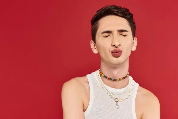 Appealing young gay man in stylish white attire with closed eyes and pounded lips on red backdrop — Stock Photo