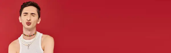 Appealing gay man in white attire posing with closed eyes and pounded lips on red backdrop, banner — Stock Photo