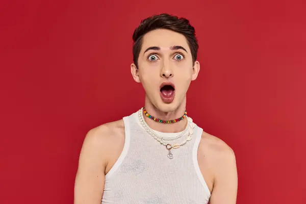 Shocked androgynous man with stylish accessories posing with hand near face and looking at camera — Stock Photo