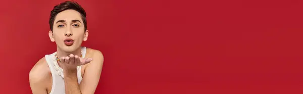 Attraente gay uomo in abbigliamento casual con accessori soffiaggio bacio a fotocamera su sfondo rosso banner — Foto stock