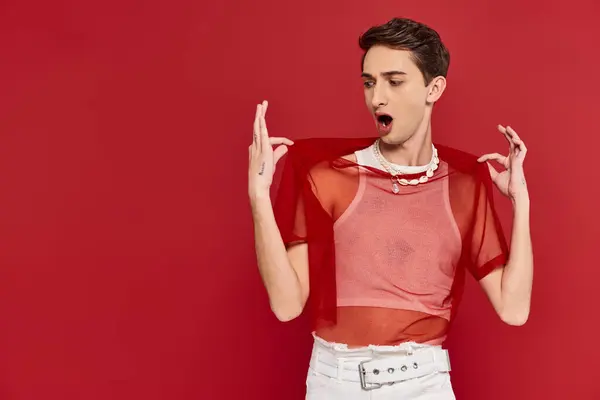 Handsome shocked androgynous man with red stylish fishnet posing emotionally on red backdrop — Stock Photo