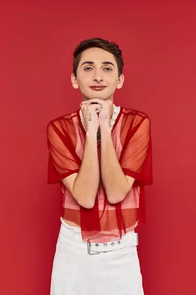 Attractive voguish androgynous man with stylish red fishnet looking at camera on red backdrop — Stock Photo