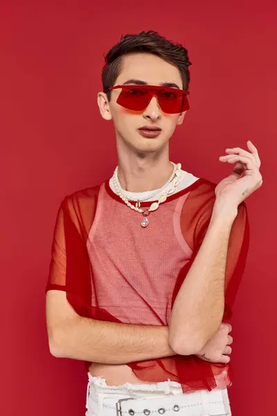 Hombre andrógino modish bien parecido con red de pescador elegante rojo y gafas de sol mirando a la cámara - foto de stock