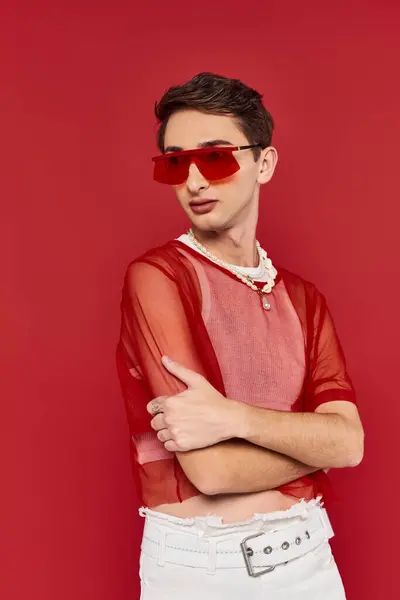 Homem andrógino sofisticado com meia-calça elegante vermelho e óculos de sol posando e olhando para longe — Fotografia de Stock