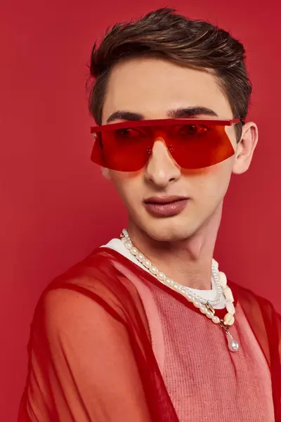 Hombre andrógino sofisticado con red de pescador elegante rojo y gafas de sol posando y mirando hacia otro lado - foto de stock