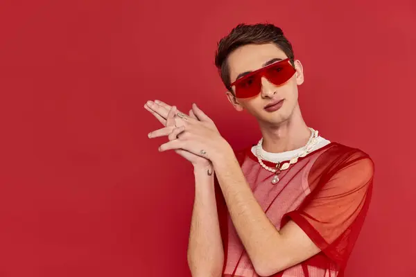 Homme androgyne bien habillé avec résille rouge élégant et lunettes de soleil posant et regardant loin — Photo de stock