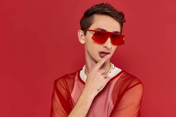 Hombre andrógino modish bien parecido con red de pescador elegante rojo y gafas de sol mirando a la cámara - foto de stock