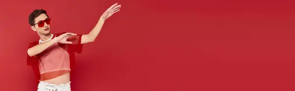 Sedutor homem andrógino com meia-calça elegante vermelho e óculos de sol posando e olhando para longe, banner — Fotografia de Stock