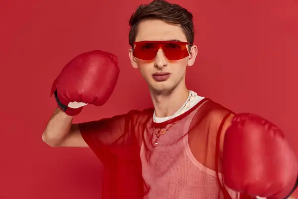 Handsome gay man with sunglasses and red fishnet posing with boxing gloves and looking at camera — Stock Photo