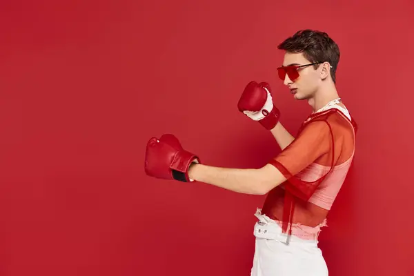 Modischer androgyner Mann mit rotem Fischnetz, der aktiv mit Boxhandschuhen posiert und wegschaut — Stockfoto