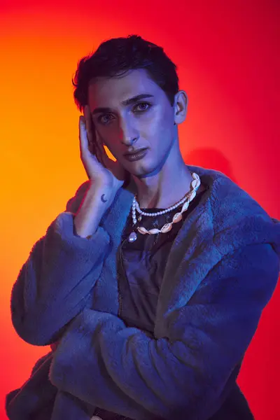 Eleganter androgyner Mann in lila Kunstpelz posiert vor lebendiger Kulisse und blickt in die Kamera — Stockfoto