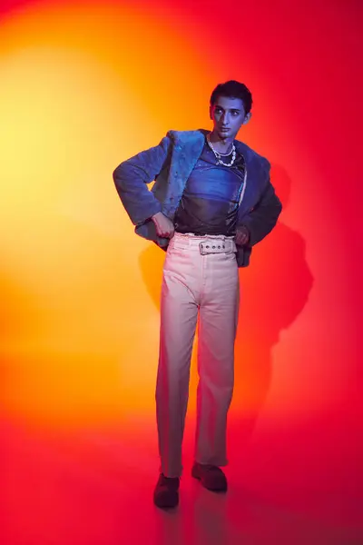 Verführerisch modisch androgyner Mann in lila Kunstpelz posiert vor lebendiger Kulisse und schaut weg — Stockfoto