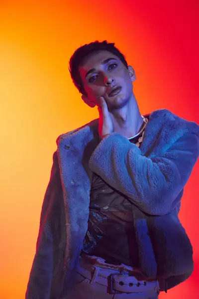 Mondäne androgyne Mann in lila Kunstpelz posiert vor lebendiger Kulisse und blickt in die Kamera — Stockfoto