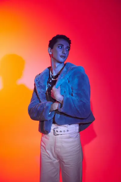 Attraente uomo androgino modish in eco-pelliccia viola in posa su uno sfondo vibrante e guardando altrove — Foto stock