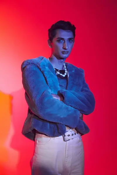Gut gekleideter androgyner Mann in lila Kunstpelz posiert vor lebendiger Kulisse und blickt in die Kamera — Stockfoto