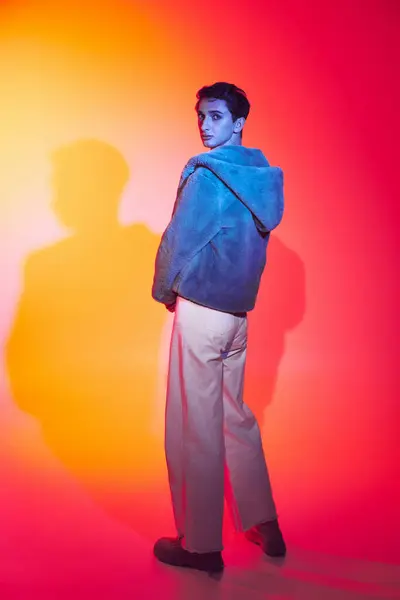 Homme androgyne bien habillé en fausse fourrure violette posant sur fond vibrant et regardant la caméra — Photo de stock