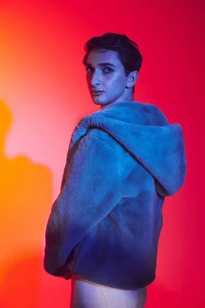 Well-dressed androgynous man in purple faux fur posing on vibrant backdrop and looking at camera — Stock Photo