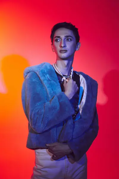 Atraente homem andrógino modish em pele de falso roxo posando em pano de fundo vibrante e olhando para longe — Fotografia de Stock