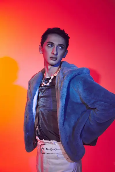 Attraktiver modisch androgyner Mann in lila Kunstpelz posiert vor lebendiger Kulisse und schaut weg — Stockfoto