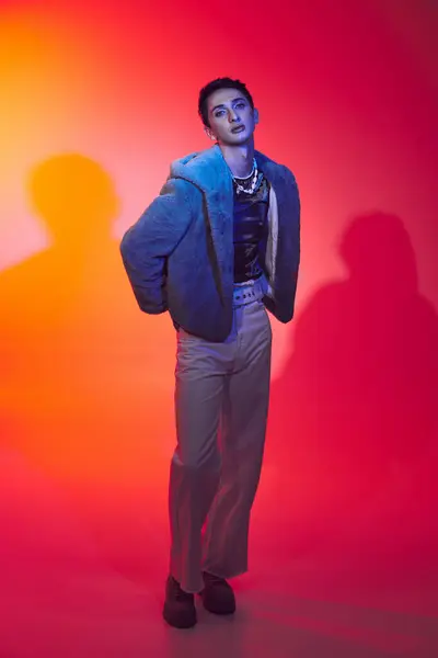 Hombre andrógino de moda en piel sintética púrpura posando sobre un vibrante telón de fondo y mirando a la cámara - foto de stock