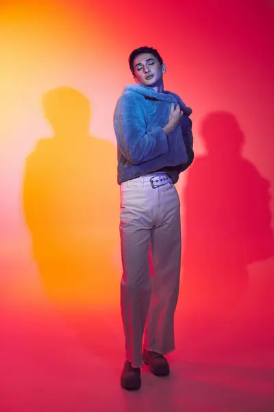 Вишуканий андрогінний чоловік у фіолетовому штучному хутрі позує із закритими очима на яскравому тлі — стокове фото
