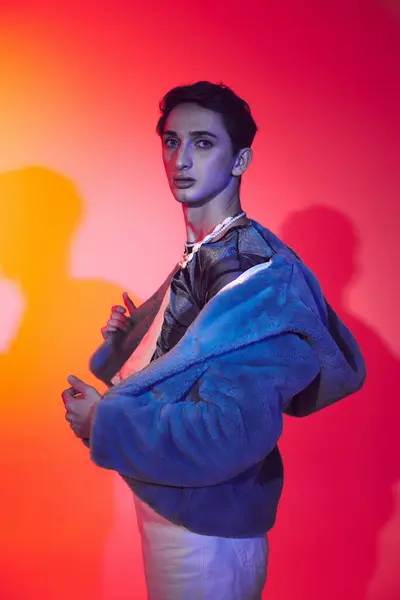 Modischer androgyner Mann in lila Kunstpelz posiert vor lebendiger Kulisse und blickt in die Kamera — Stockfoto
