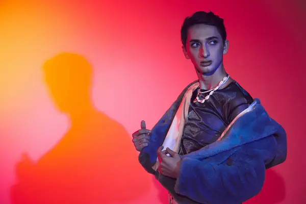 Schöner modisch androgyner Mann in lila Kunstpelz posiert vor lebendiger Kulisse und schaut weg — Stockfoto