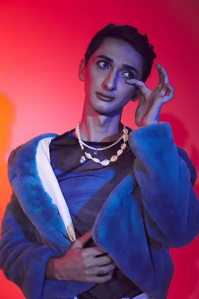 Schöner modisch androgyner Mann in lila Kunstpelz posiert vor lebendiger Kulisse und schaut weg — Stockfoto
