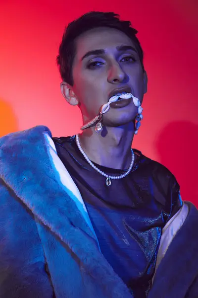 Modischer androgyner Mann in lila Kunstpelz posiert vor lebendiger Kulisse und blickt in die Kamera — Stockfoto