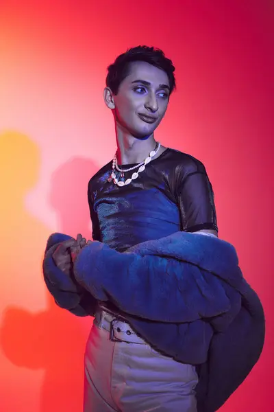 Gut aussehender modisch androgyner Mann in lila Kunstpelz posiert vor lebendiger Kulisse und schaut weg — Stockfoto