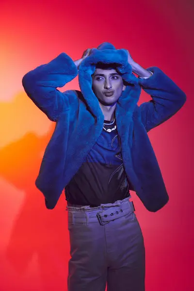 Gut aussehender stilvoller schwuler Mann in modischem lila Kunstpelz vor lebendiger Kulisse und wegschauen — Stockfoto