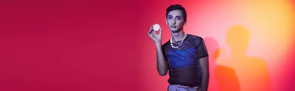Good looking gay man in casual vivid attire holding cream in his hands and looking at camera, banner — Stock Photo