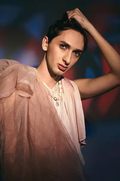 Fancy androgynous fashionista with dark hair in pastel attire looking at camera on vivid backdrop — Stock Photo