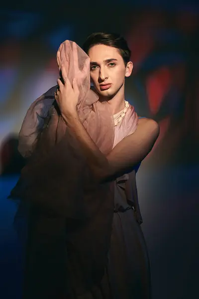 Seductor andrógino fashionista con el pelo oscuro en traje de pastel mirando a la cámara en el fondo vívido - foto de stock