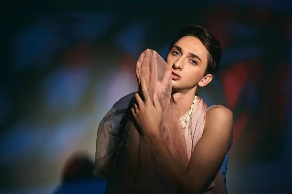 Verführerische androgyne Fashionista mit dunklen Haaren in pastellfarbener Kleidung, die vor lebendigem Hintergrund in die Kamera blickt — Stockfoto