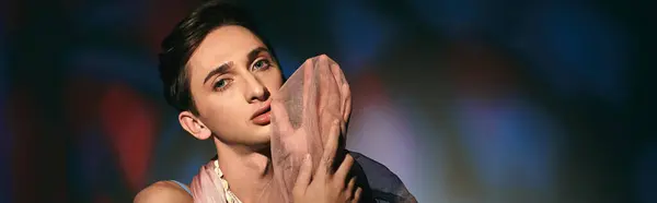 Schicker androgyner Mann mit dunklen Haaren in pastellfarbener Kleidung, der vor lebendigem Hintergrund in die Kamera blickt, Banner — Stockfoto