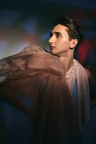 Elegante hombre andrógino bien vestido en ropa elegante pastel mirando hacia otro lado en el vibrante telón de fondo - foto de stock