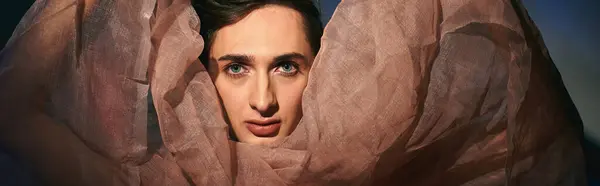 Chic androgynous man with dark hair in pastel attire looking at camera on vivid backdrop, banner — Stock Photo