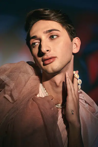 Schicker androgyner Mann in pastellfarbener eleganter Kleidung, der vor lebendiger Kulisse wegschaut — Stockfoto