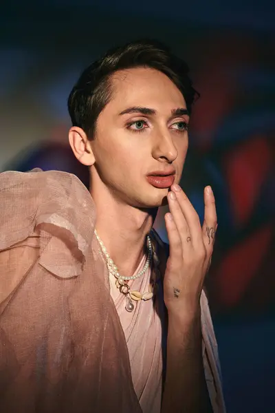 Schicker androgyner Mann in pastellfarbener eleganter Kleidung, der vor lebendiger Kulisse wegschaut — Stockfoto