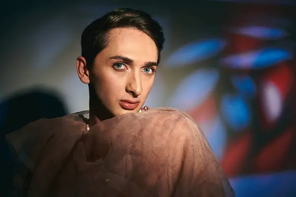 Anspruchsvolle androgyne Fashionista in pastellfarbener Kleidung blickt vor vibrierender Kulisse in die Kamera — Stockfoto