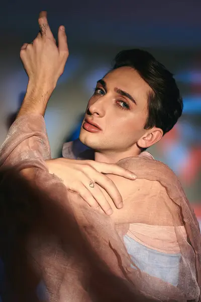 Elegant androgynous fashionista with dark hair in pastel attire looking at camera on vivid backdrop — Stock Photo