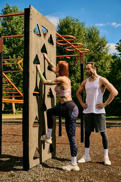A woman in sportswear, guided by a personal trainer, climbing a rock wall, showcasing determination and motivation. — Stock Photo
