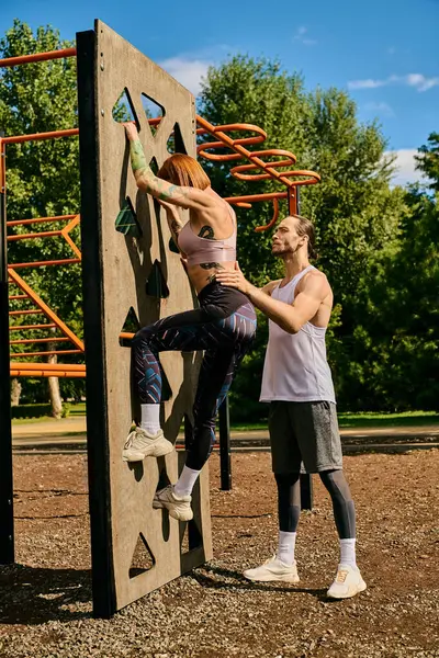 Una donna determinata, in abbigliamento sportivo, scalando una parete rocciosa all'aperto con personal trainer, mostrando motivazione e lavoro di squadra. — Foto stock