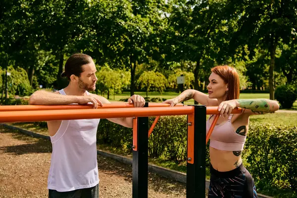 Un uomo e una donna in abbigliamento sportivo stanno fianco a fianco all'aperto, concentrandosi sulla loro routine di esercizio, guidati da un personal trainer.. — Foto stock