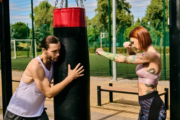 Una donna in abbigliamento sportivo si impegna in un allenamento di pugilato in un parco, guidata da un personal trainer, mostrando determinazione e motivazione.. — Foto stock