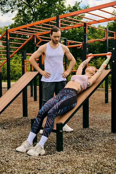 Определенный мужчина и женщина в спортивной одежде уверенно стоят на деревянной скамейке во время сложной тренировки на открытом воздухе. — стоковое фото