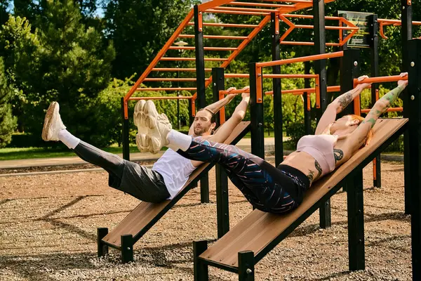 A man and woman in sportswear lay on benches exercising with a personal trainer, showcasing determination and motivation. — Stock Photo