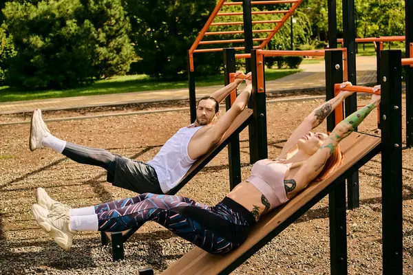 Un hombre y una mujer en ropa deportiva están acostados en un banco al aire libre, tomando un descanso después de hacer ejercicio con un programa personal. - foto de stock
